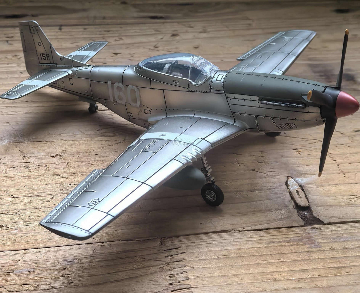 Detailed silver die-cast scale model of a vintage WWII fighter aircraft on a wooden surface.